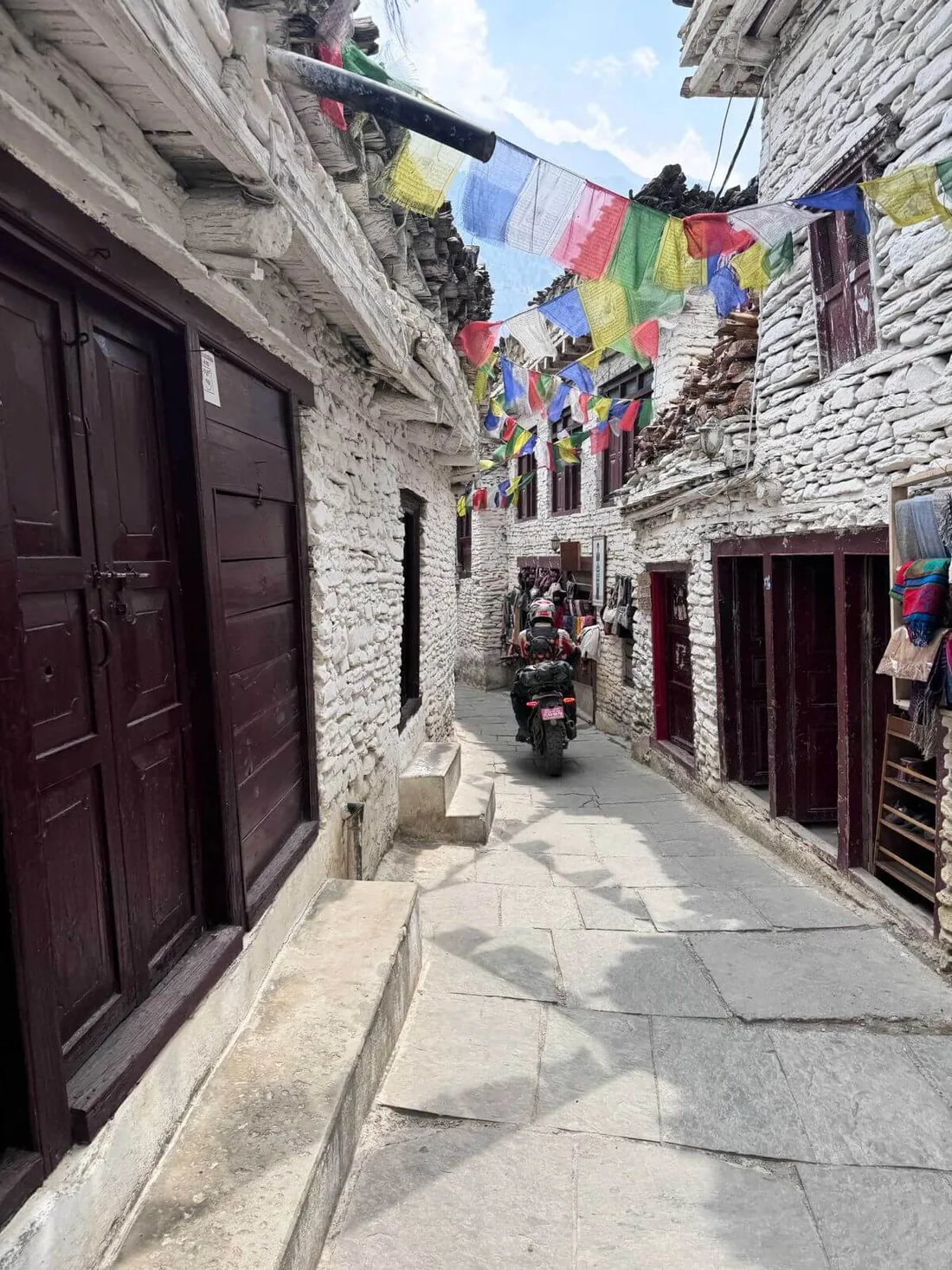 Motards traversant une ruelle de pierre sous des drapeaux de prières